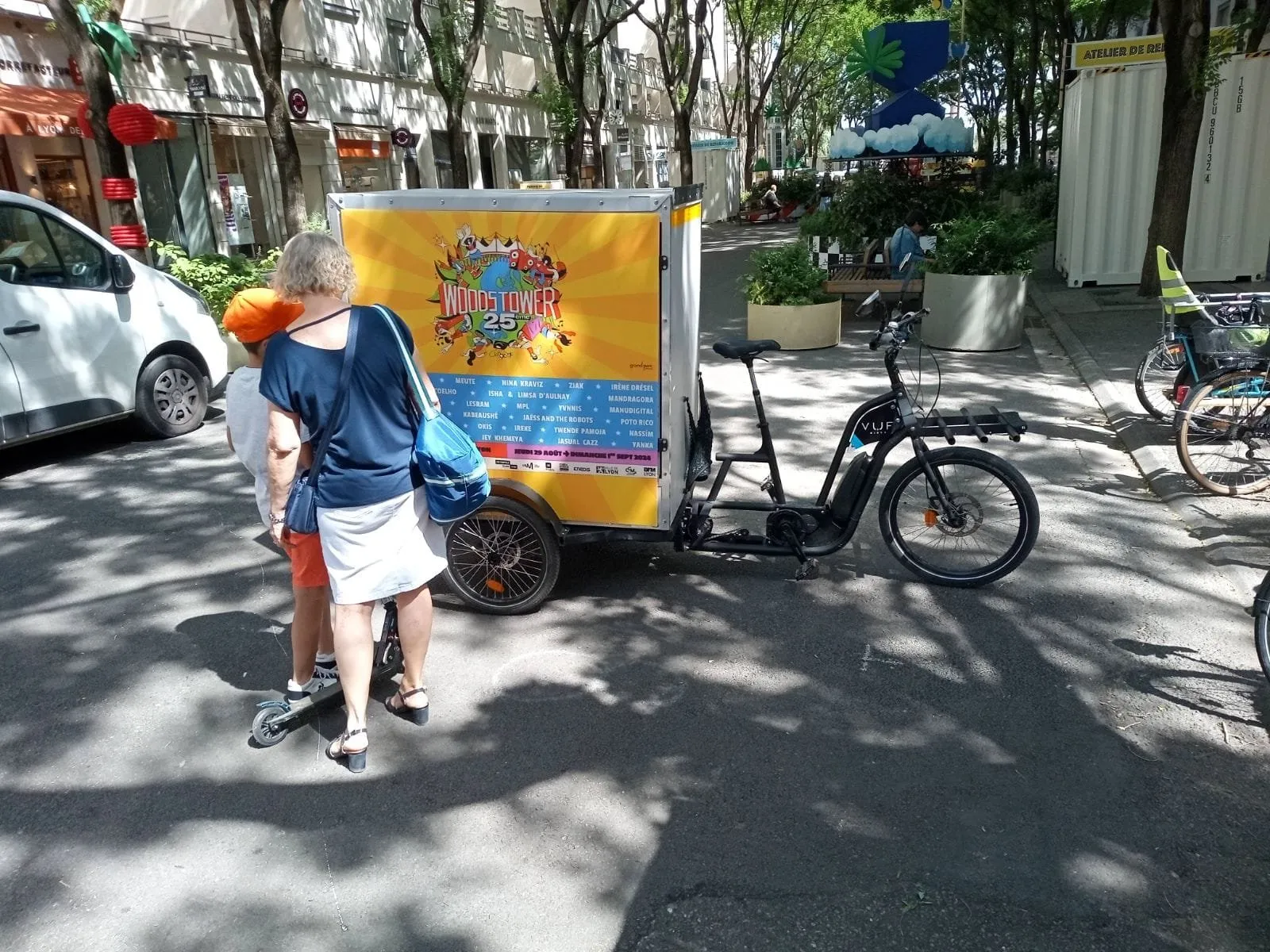 Triporteur publicitaire aux couleurs d’un festival dans une rue arborée animée